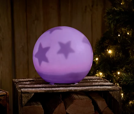 Boule violette avec des étoiles sur une caisse en bois à côté d'un arbre de Noël.