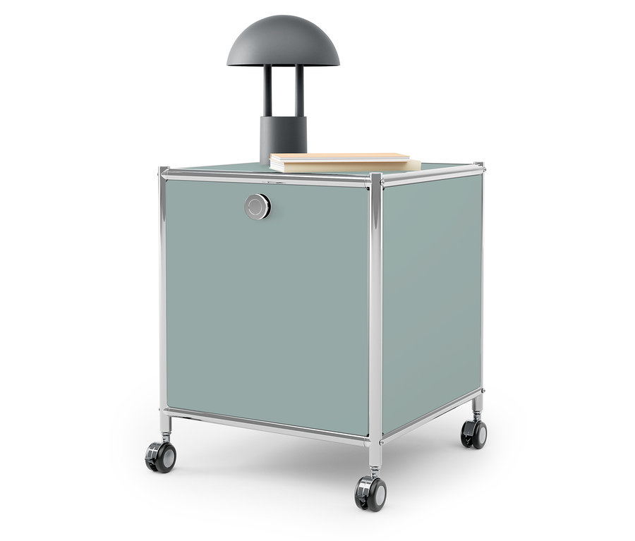 Lampe grise et livre sur une boîte de rangement bleu-vert sur roulettes.