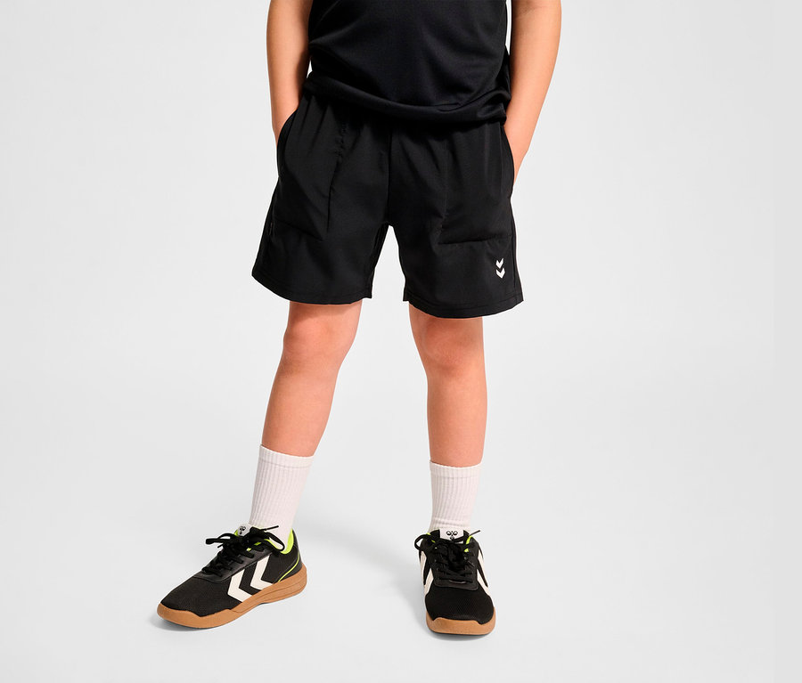 Un garçon portant un short d’entraînement HUMMEL HMLJR Pulse noir, des chaussettes blanches et des baskets.