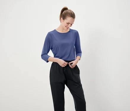 Une femme ajuste son pantalon noir avec un t-shirt bleu à manches trois-quarts.