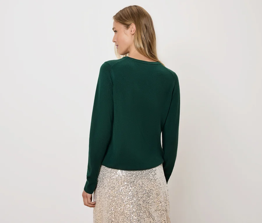 Femme regardant par-dessus son épaule portant un pull vert et une jupe à paillettes.