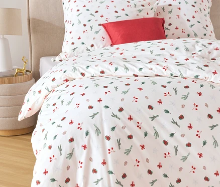 Linge de lit blanc avec des motifs rouges et verts et un coussin rouge sur un lit.
