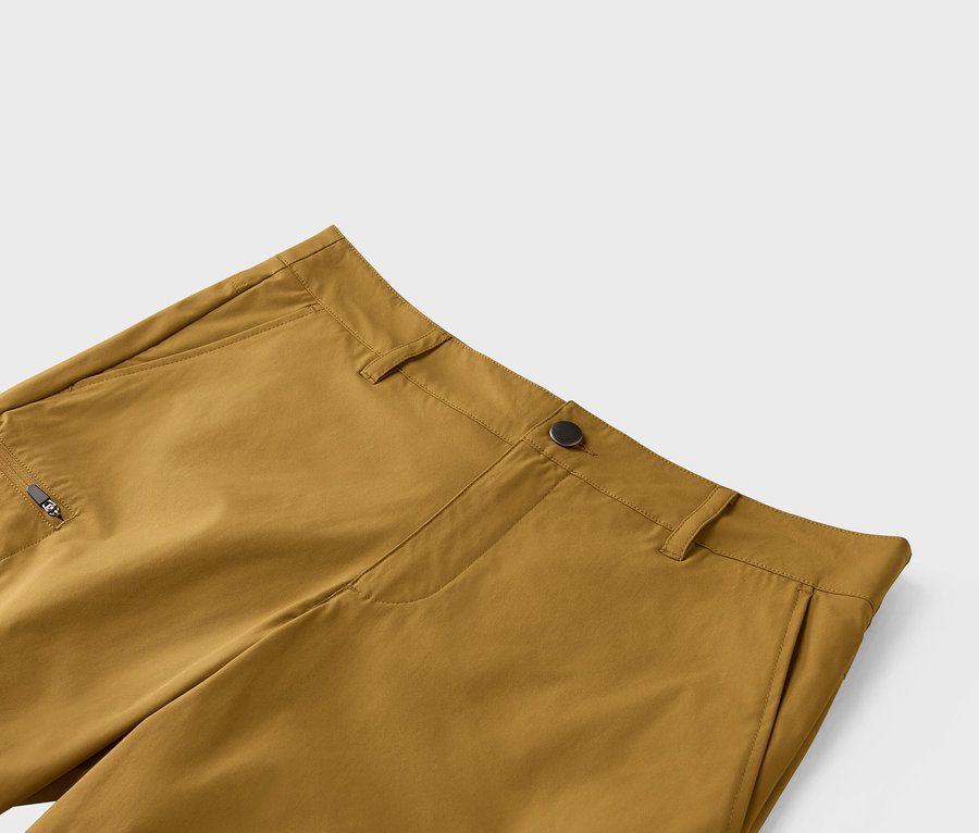 Gros plan d'un pantalon ocre avec fermeture à bouton et poche zippée.