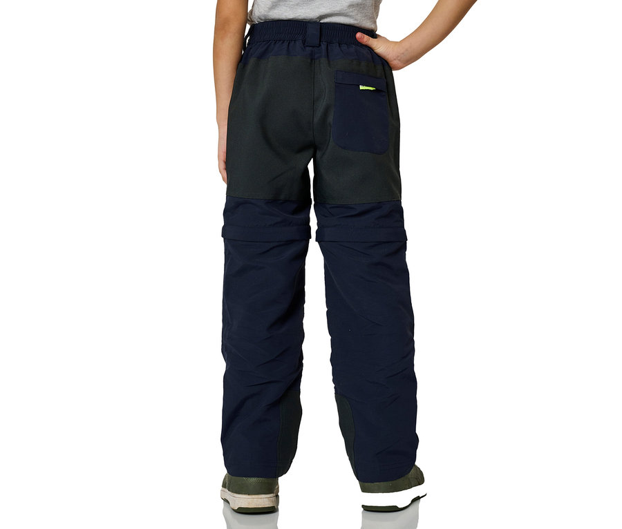 Enfant de dos, portant un Pantalon zip-off JAKO-O bicolore marine et gris foncé avec un détail vert fluo sur la poche arrière.