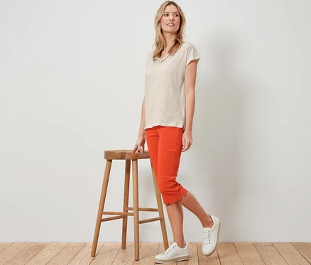 Blonde posant à côté d'un tabouret en bois en pantalon 3/4 stretch orange.