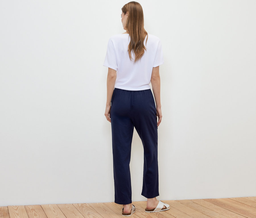 Une femme, vue de dos, porte un pantalon en lin bleu foncé, un t-shirt blanc et des sandales.