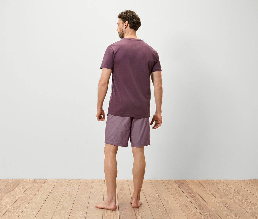 Un homme se tient dos à la caméra portant un t-shirt violet et un short.
