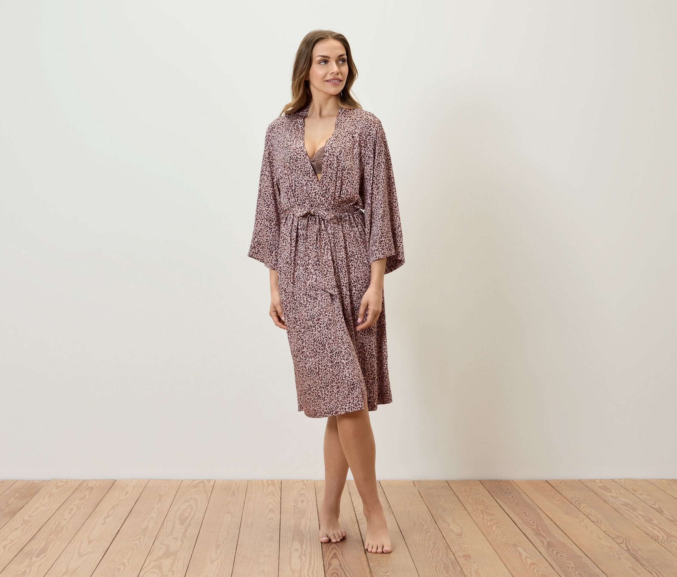 Une femme se tient sur un plancher en bois et porte un peignoir à motifs.