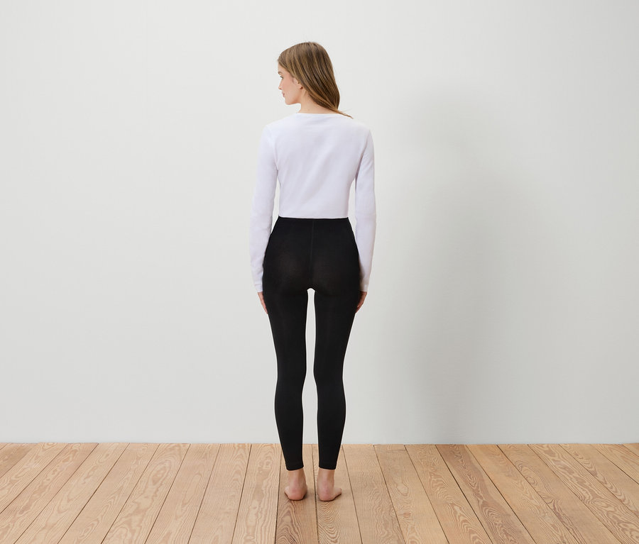 Une femme, vue de dos, porte un t-shirt blanc à manches longues et un legging noir.