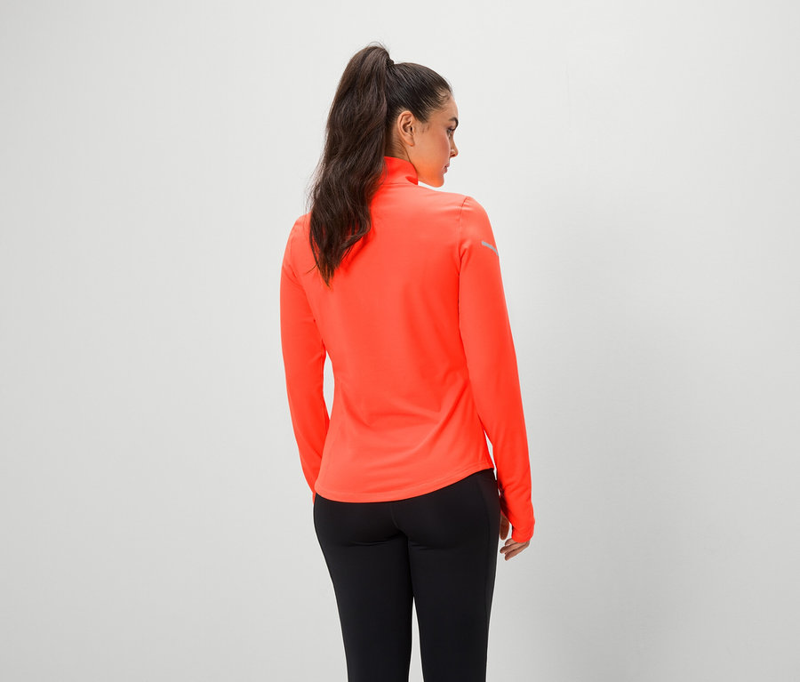 Une femme, dos à la caméra, porte un haut orange à manches longues et un legging noir.