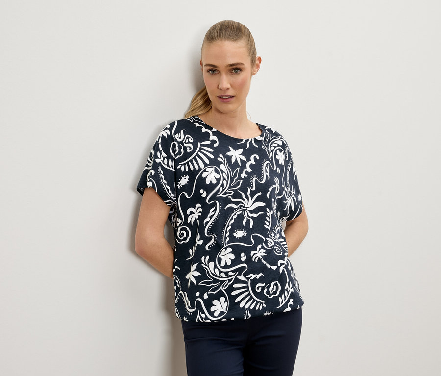 Femme blonde portant un chemisier bleu marine à motifs blancs.
