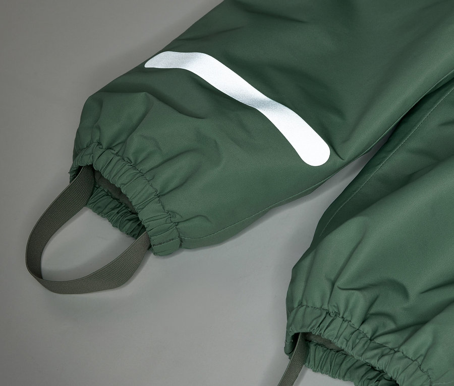 Gros plan sur un pantalon de pluie vert avec des poignets élastiques et une bande réfléchissante sur la jambe.