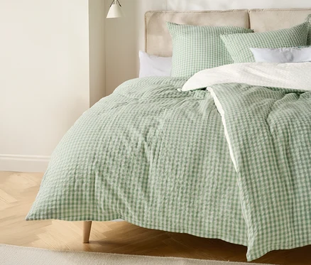Un lit avec une couette à carreaux vert clair et blanc et des coussins assortis.
