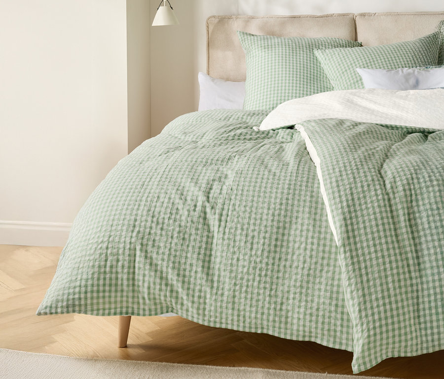 Un lit avec une couette à carreaux vert clair et blanc et des coussins assortis.