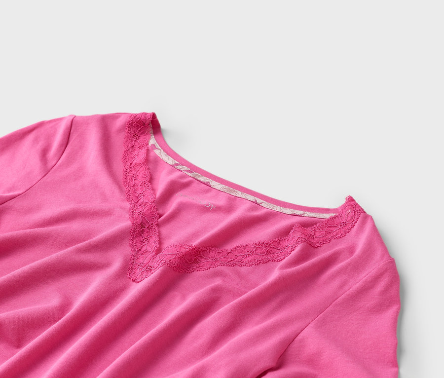 Gros plan d'un t-shirt rose à col en V et bordure en dentelle sur fond blanc.