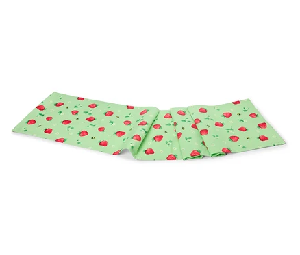 Un chemin de table vert clair avec des fraises et des abeilles est plié sur un fond blanc.