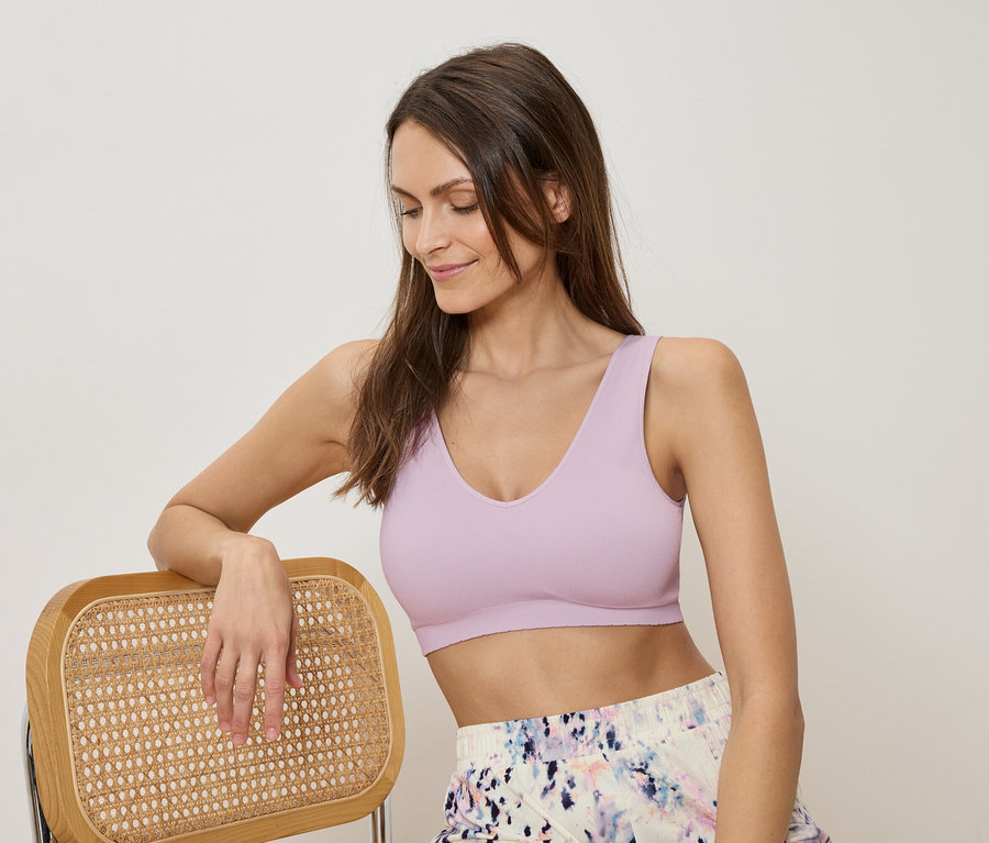 Femme appuyée sur une chaise portant un soutien-gorge de sport violet et un short à motifs.