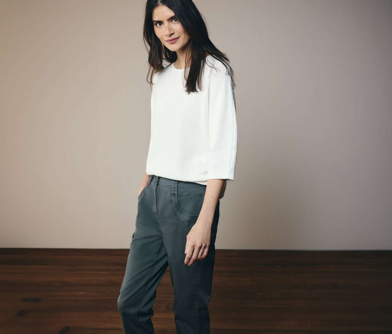 Une femme portant un haut blanc et un pantalon CECIL « Scarlett » vert foncé pose devant un fond clair.