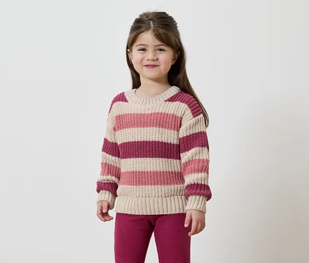 Une fille aux cheveux bruns porte un pull rayé rose, beige et bordeaux et un pantalon bordeaux sur fond blanc.