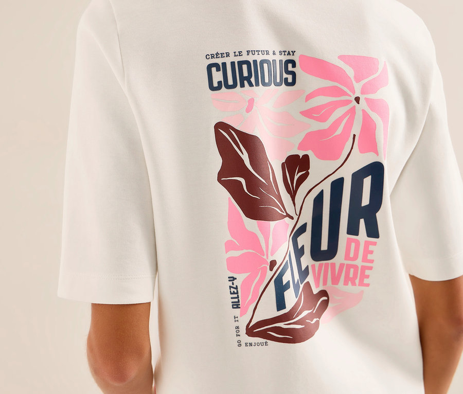 Personne de dos portant un sweatshirt CECIL blanc avec un imprimé graphique coloré au dos. L'imprimé présente des fleurs roses, des feuilles marron et les textes « CRÉER LE FUTUR & STAY CURIOUS » et « FLEUR DE VIVRE ».