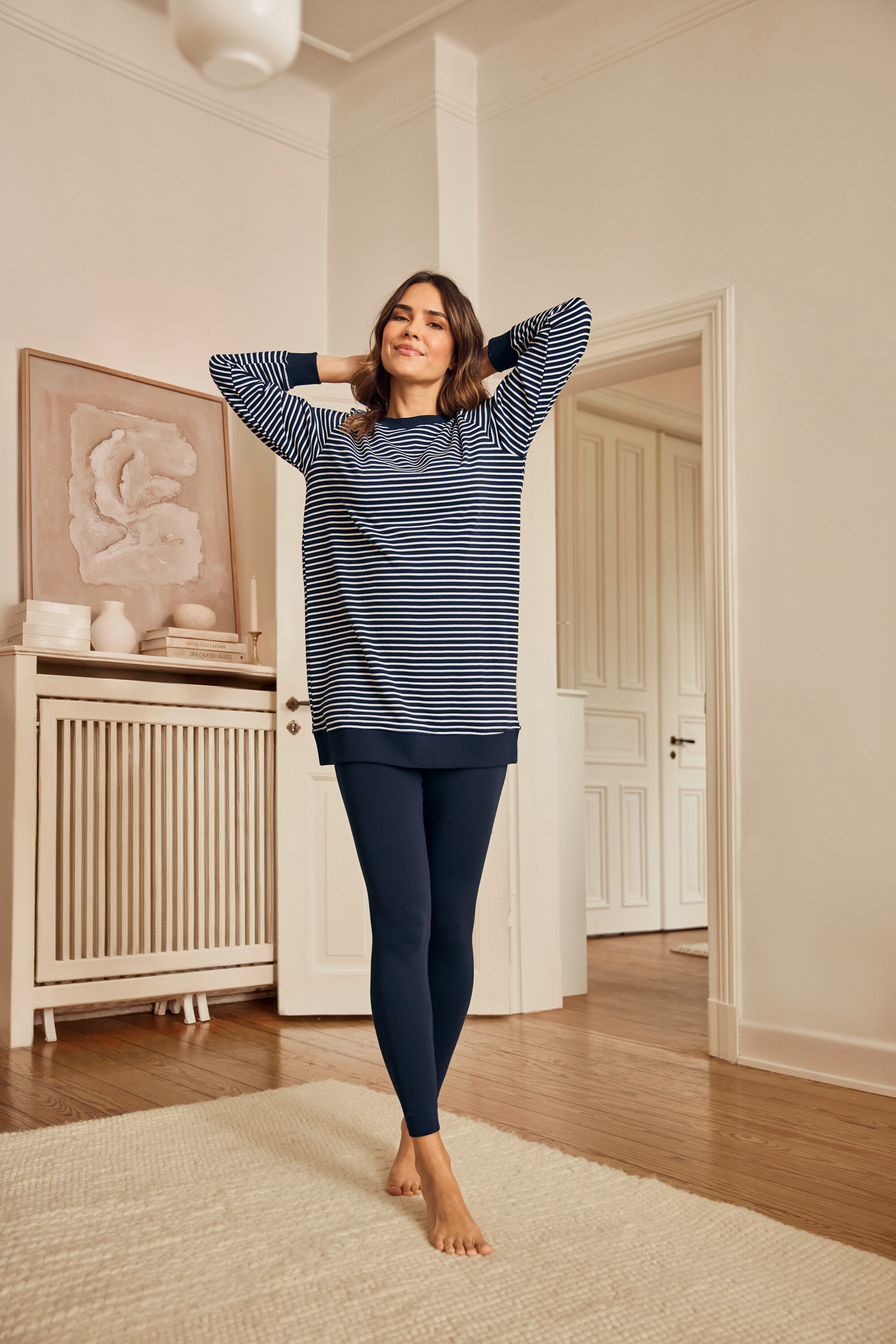 Femme portant un pyjama legging, debout pieds nus sur un tapis.