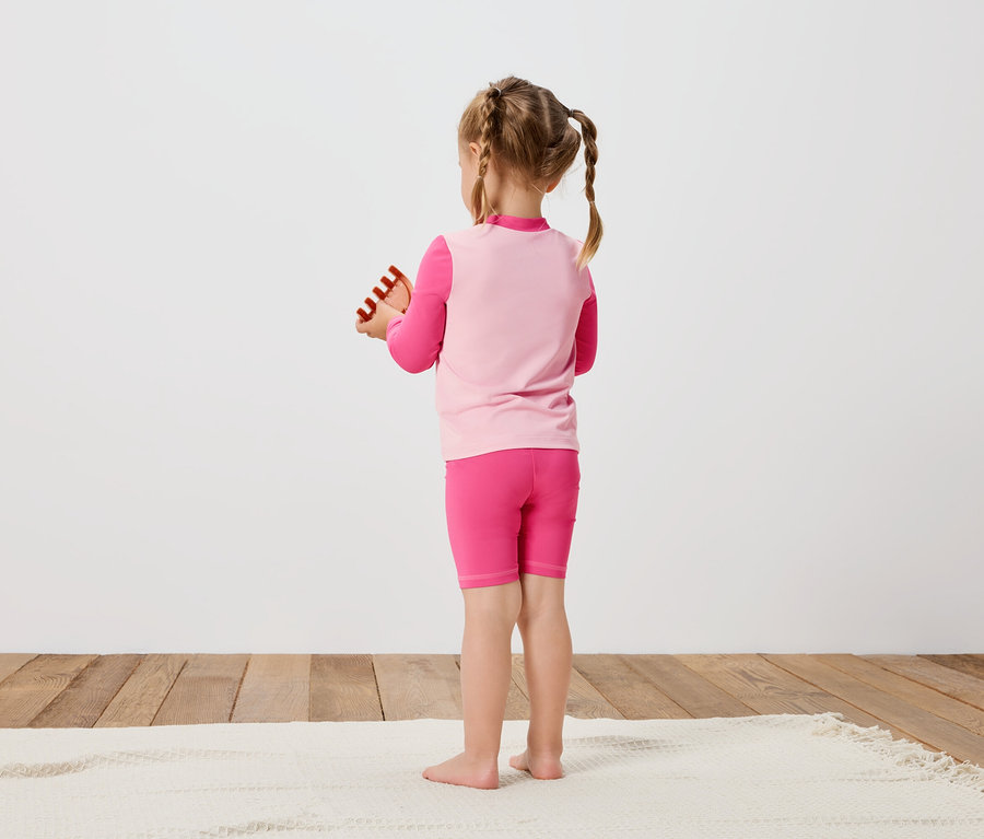 Fillette vue de dos en tenue de sport rose, tenant un jouet dans ses mains.