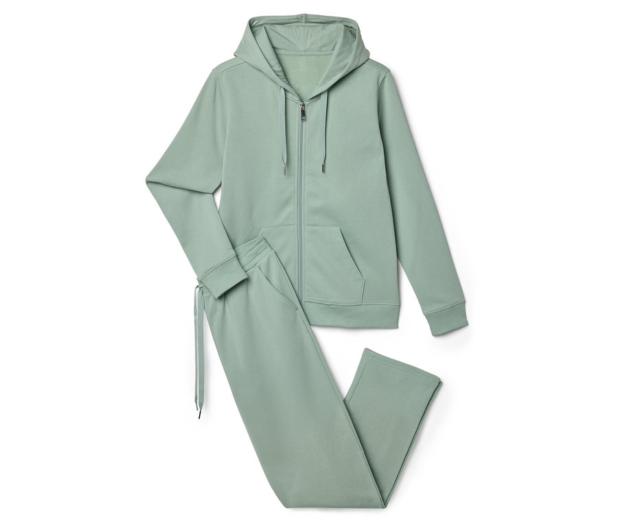 Un survêtement vert clair composé d'un sweat à capuche zippé et d'un pantalon de jogging est posé sur un fond blanc.