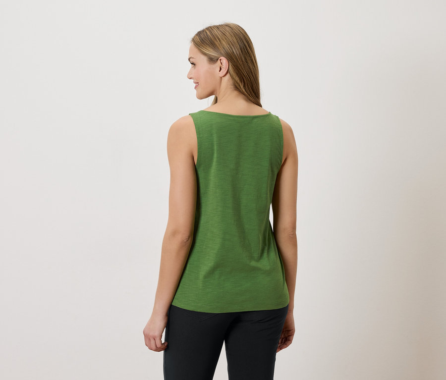 Femme de dos, portant un débardeur vert et un pantalon noir sur fond blanc.