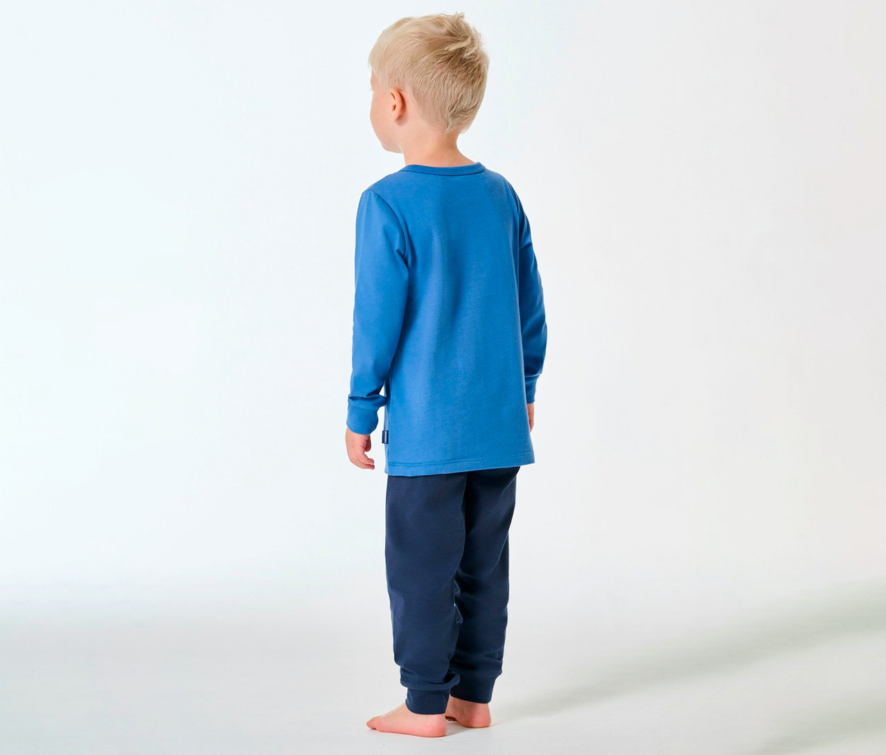 Garçon vu de dos, pieds nus, portant un pyjama long pour enfant SCHIESSER bleu.