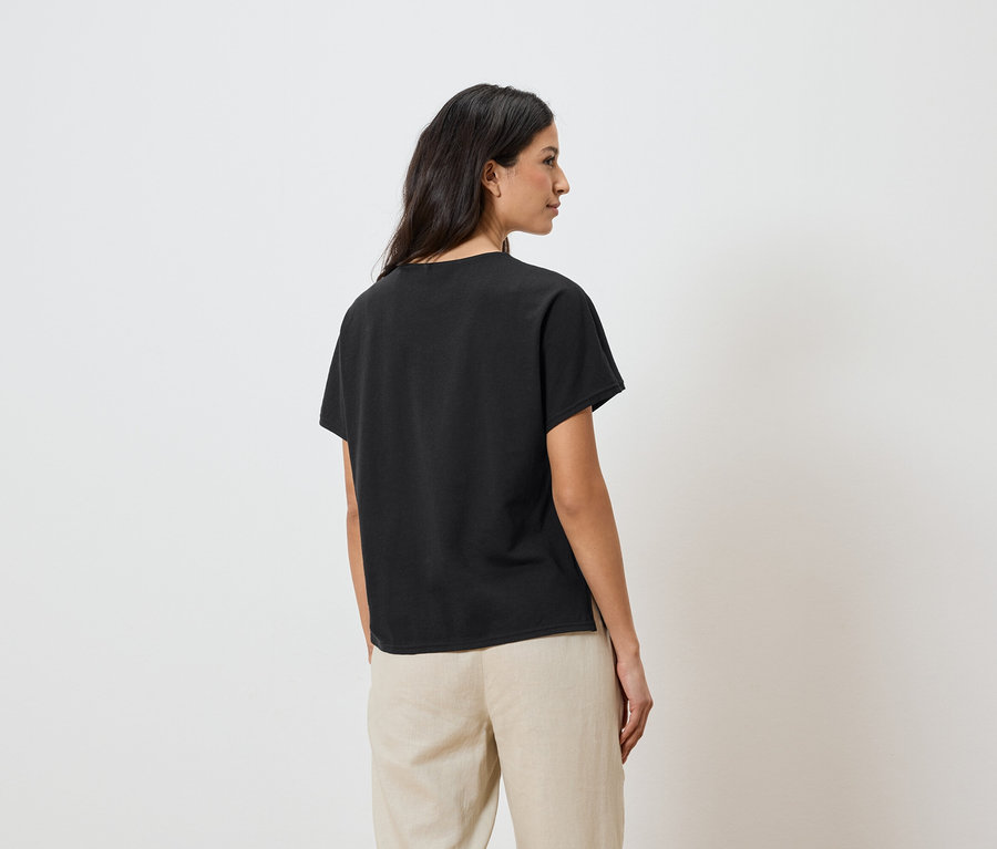 Femme portant un t-shirt noir et un pantalon beige.