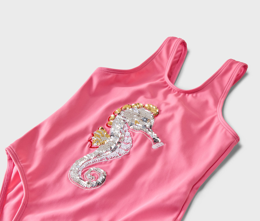 Gros plan d'un maillot de bain rose avec un motif de paillettes d'hippocampe argenté et doré.