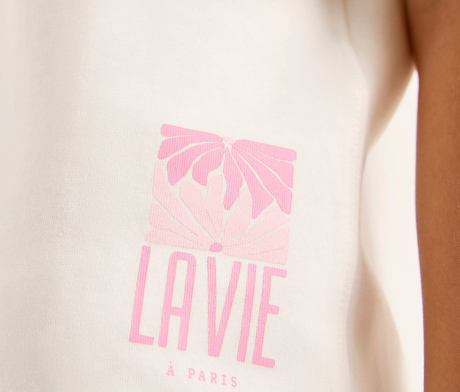 Gros plan d'un sweatshirt CECIL blanc avec un imprimé graphique rose représentant une fleur stylisée au-dessus de « LAVIE » et « À PARIS », porté par une personne.