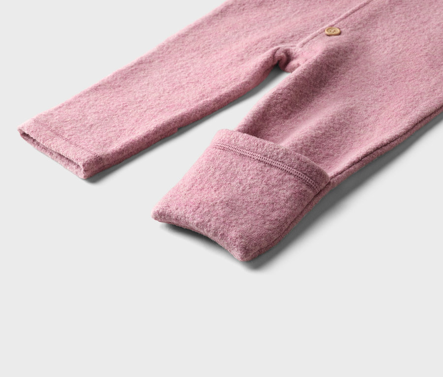 Gros plan d'une barboteuse bébé rose en tissu texturé avec un revers sur la jambe et un bouton.