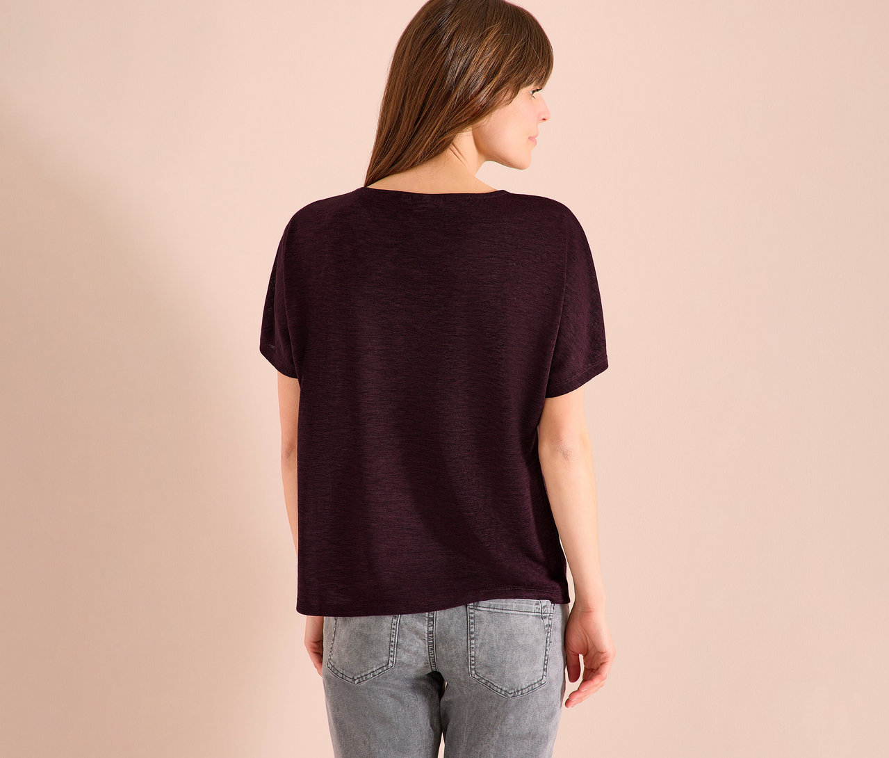 Vue arrière d'une femme aux cheveux bruns portant un t-shirt bordeaux et un jean gris.