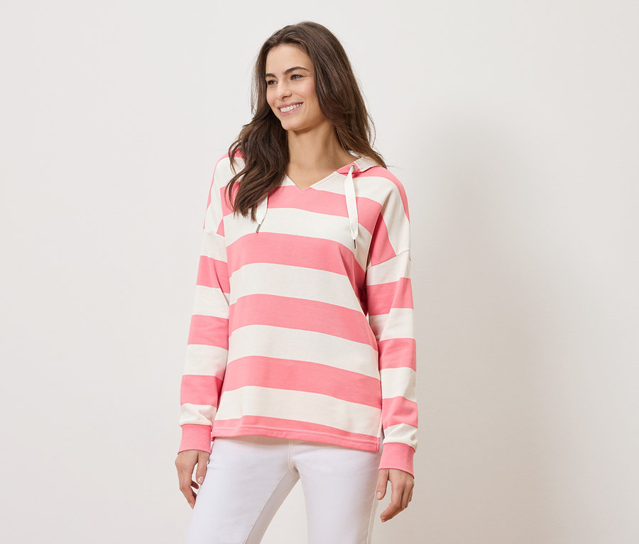 Femme portant un sweat à capuche rayé rose et blanc et un pantalon blanc.