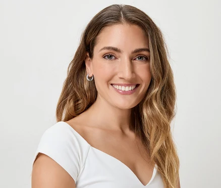 Une femme souriante aux longs cheveux bruns ondulés et portant des boucles d'oreilles.
