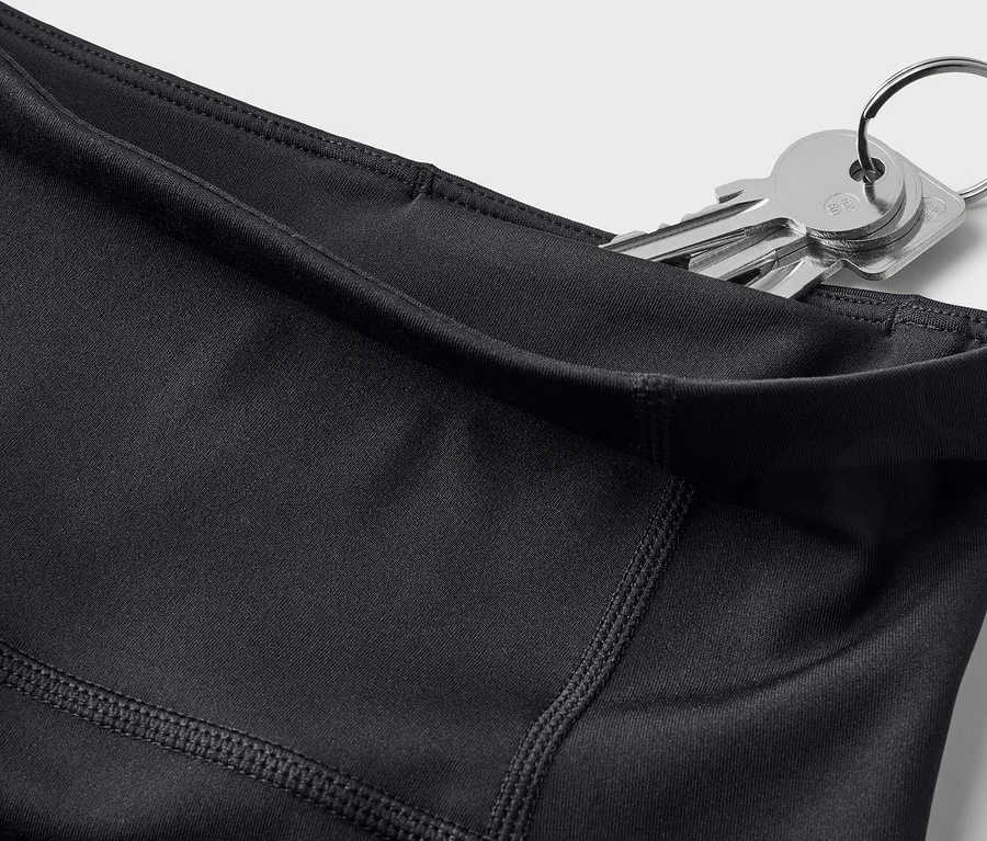 Gros plan d'un legging noir avec des clés dans la poche sur fond blanc.