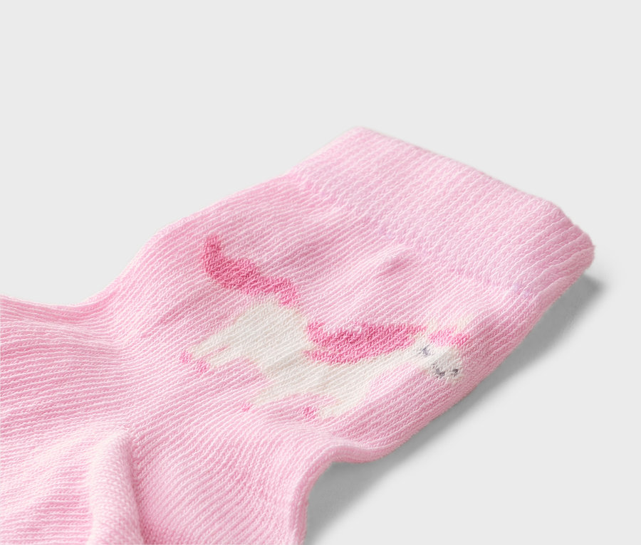 Gros plan d'une chaussette rose clair avec une licorne blanche à la crinière et à la queue roses.