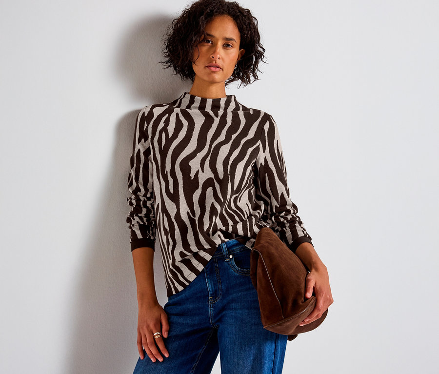 Femme portant un maillot en jacquard Street One à motif zébré, un jean et tenant un sac marron.