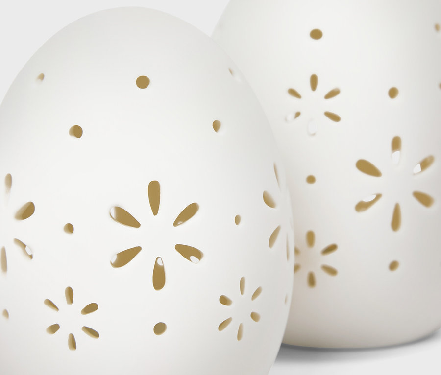 Deux décorations en céramique blanches en forme d'œuf avec des motifs de fleurs et de points découpés.
