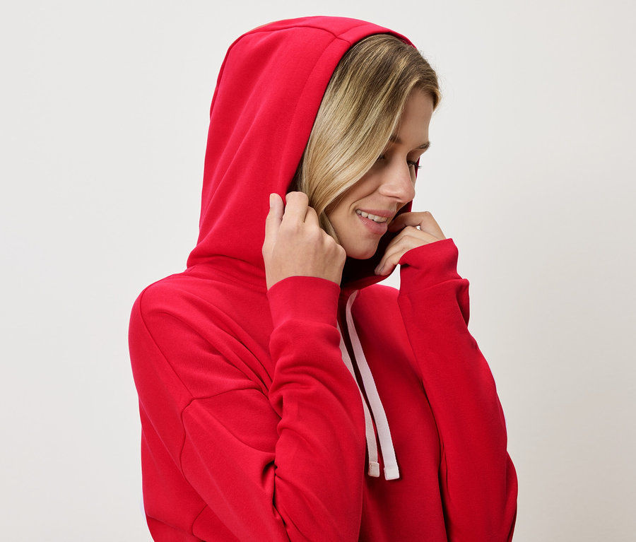 Une femme blonde porte un sweat à capuche rouge et tient la capuche.