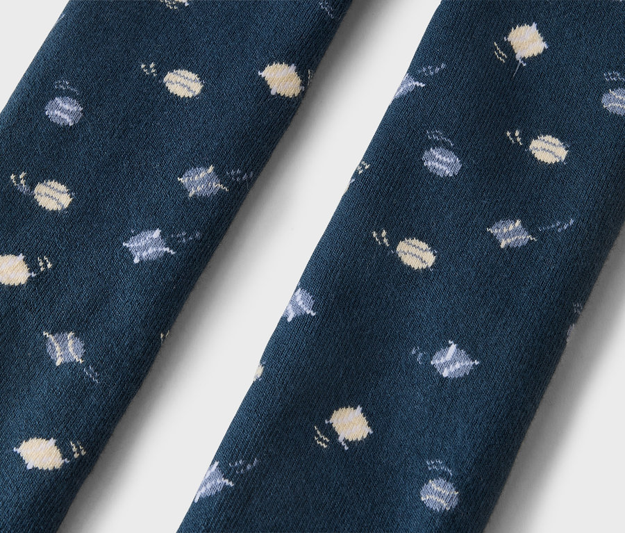 Gros plan de deux sections de tissu bleu foncé, probablement des chaussettes, présentant un motif répétitif de petites planètes et étoiles jaune clair et grises.