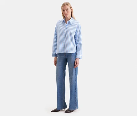 Une femme porte un chemisier oversize Seidensticker rayé bleu et blanc avec un jean bleu.