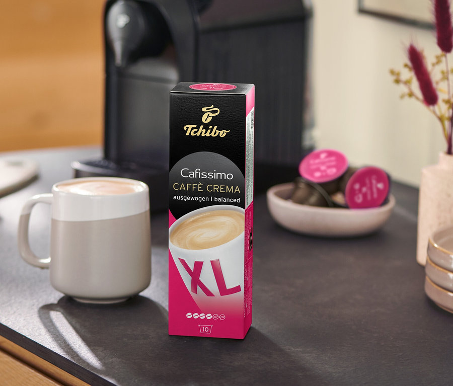 Une machine à café est posée sur un comptoir de cuisine à côté d'un paquet de capsules Caffè Crema Wake Up XL – 80 et d'une tasse.