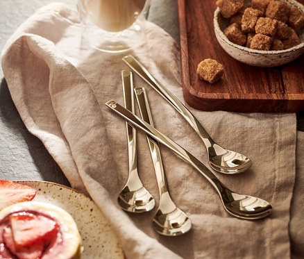 Verre de latte macchiato, à côté d'un bol de sucre brun et d'une tartelette aux fraises. Sur la serviette se trouve un lot de 4 cuillères à latte macchiato.