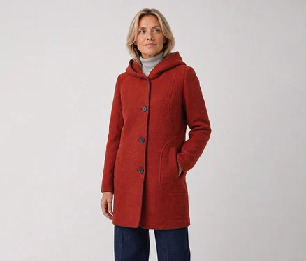 Femme portant un manteau rouge à capuche et un jean bleu foncé, debout, la main droite dans la poche du manteau et regardant vers la droite.