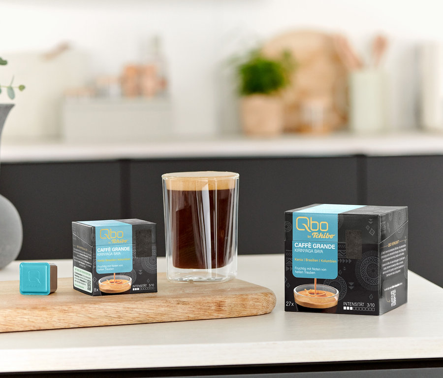 Sur une table, il y a une tasse de café, un Qbo Caffè Grande KIRINYAGA BAYA – 8 capsules et un Qbo Caffè Grande KIRINYAGA BAYA – 27 capsules.