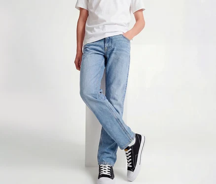 Personne portant un t-shirt blanc, un jean Jack&Jones JJOriginal Chris bleu clair et des baskets noires, appuyée contre un bloc blanc, jambes croisées.