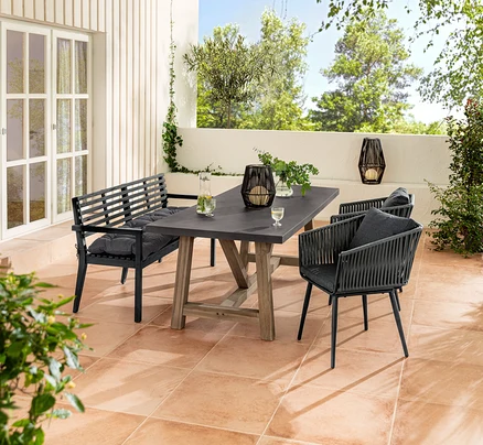 Un ensemble de meubles de jardin avec un banc de jardin et un coussin Sun Garden, une table à manger, des fauteuils avec tressage textile et une lanterne solaire.