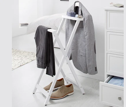 Sur un fond blanc, un valet de nuit sur lequel sont suspendus un blazer gris et un pantalon, et des chaussures marron sont placées en dessous.